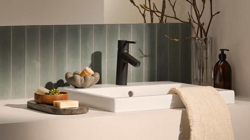 Bathroom sink with black faucet, soap, and towel on a tiled wall background