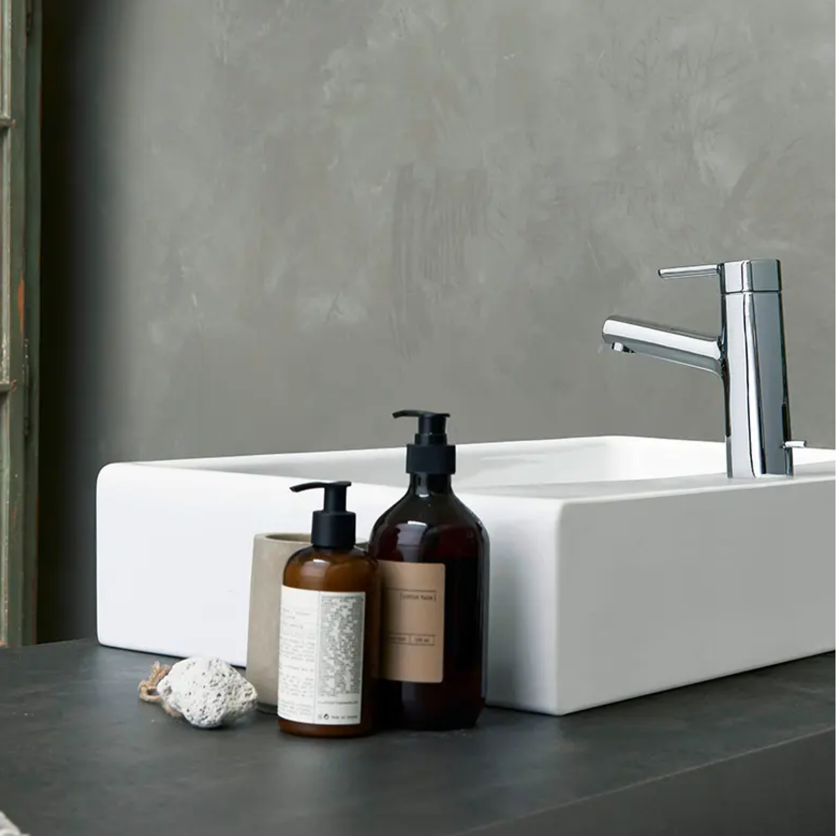 Bathroom setting with a white sink, silver faucet, and two brown bottles on a dark surface.